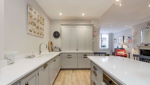 A modern kitchen with white cabinetry, a large island, and a dining area with a red chair. - Divine Mews House - South Kensington (London)