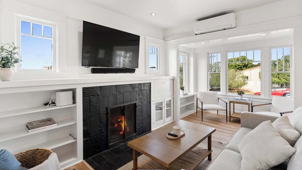 A modern living room with a fireplace, a flat-screen TV, white furniture, and large windows. - Steps to La Jolla Cove - Private Outdoor Oasis (San Diego)