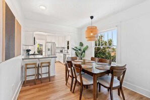 Una cocina moderna con armarios blancos, un comedor con una mesa y sillas de madera, y un amplio ventanal con vistas a la vegetación.