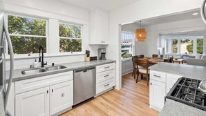 A modern kitchen with white cabinetry, a dishwasher, and a dining area with a table and chairs. - Steps to La Jolla Cove - Private Outdoor Oasis (San Diego)