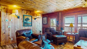 A cozy cabin interior with wooden walls, leather furniture, and a large window offering a view. - Pamoola Lodge - Waterfront| sleeps 11+|Private Dock (Rockwood)
