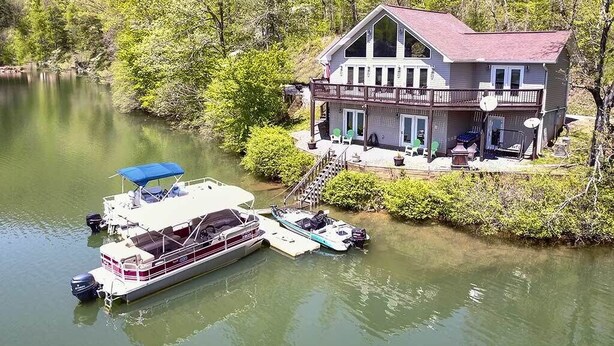 Una casa frente al lago con un muelle, un bote y un porche cubierto.