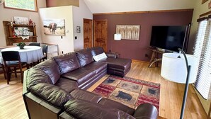 Una sala de estar con sofá modular, televisor, comedor con mesa y sillas, y ventilador de techo.