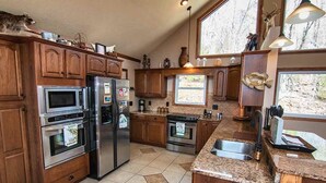 Una cocina con armarios de madera, electrodomésticos de acero inoxidable, encimera de granito y una ventana con vistas a árboles.