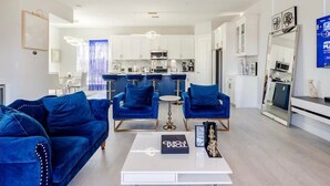 A modern living room with a sofa, coffee table, and a kitchen in the background. - Villa De Briley - Downtown HTX - Fire Pit - Photo Booth!
Luxury Family Retreat (Houston)