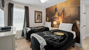 A hotel room with two beds, a ceiling fan, a large Hogwarts-themed wall mural, a desk with a computer, and a window with curtains. - Cuban Palms Paradise | Theatre & Games - Luxe Resort + 10 Min Disney + Pet Friendly (Kissimmee)