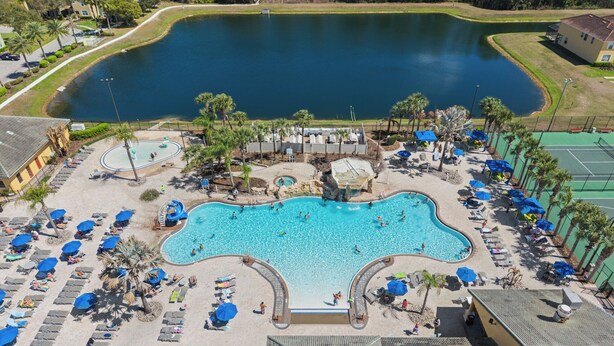 A large swimming pool with multiple lanes, surrounded by lounge chairs and umbrellas, and a smaller pond nearby. - Cuban Palms Paradise | Theatre & Games - Luxe Resort + 10 Min Disney + Pet Friendly (Kissimmee)