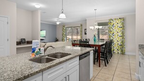 A kitchen with granite countertops, a sink, and a dishwasher. There is a dining area with a table and chairs. - Cuban Palms Paradise | Theatre & Games - Luxe Resort + 10 Min Disney + Pet Friendly (Kissimmee)