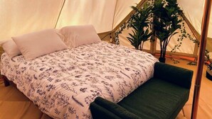 Una carpa con una cama, almohadas, un banco verde y plantas en macetas.