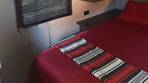 A compact room with a bed, a mounted TV, a shelf with a red vase, and a window with blinds. - Lovely 1-bedroom recreational vehicle with AC in Sacramento near Rancho Cordova (Sacramento)