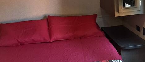 A bed with red bedding, a small bedside table, and a mirror on the wall.