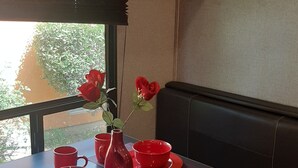 A table with red tableware and a vase with a red flower, a window with a view of greenery, and a wall-mounted control panel. - Lovely 1-bedroom recreational vehicle with AC in Sacramento near Rancho Cordova (Sacramento)