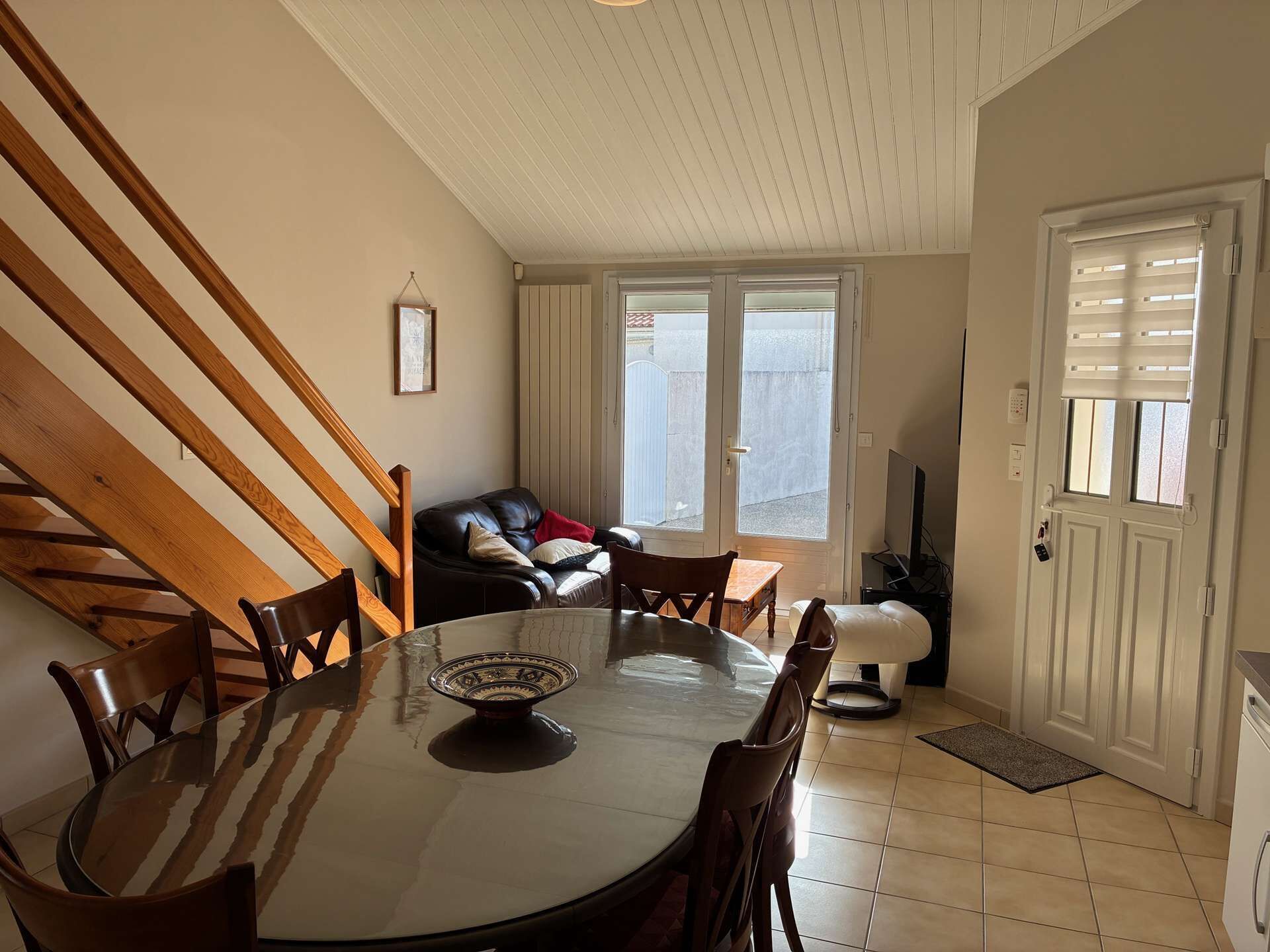 A dining area with a round table, chairs, a sofa, a TV, and a door with windows.