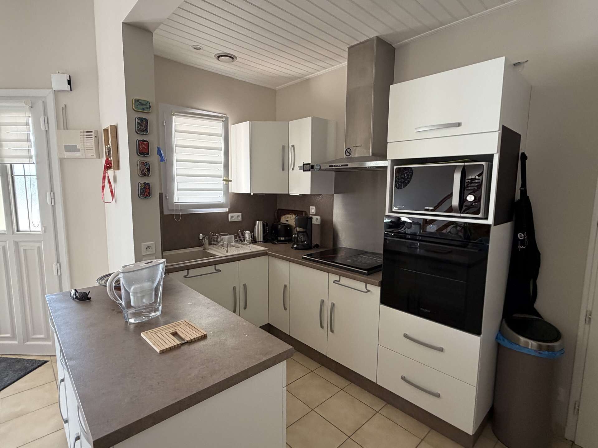 A modern kitchen with white cabinets, a stainless steel range hood, a built-in oven, and a microwave.
