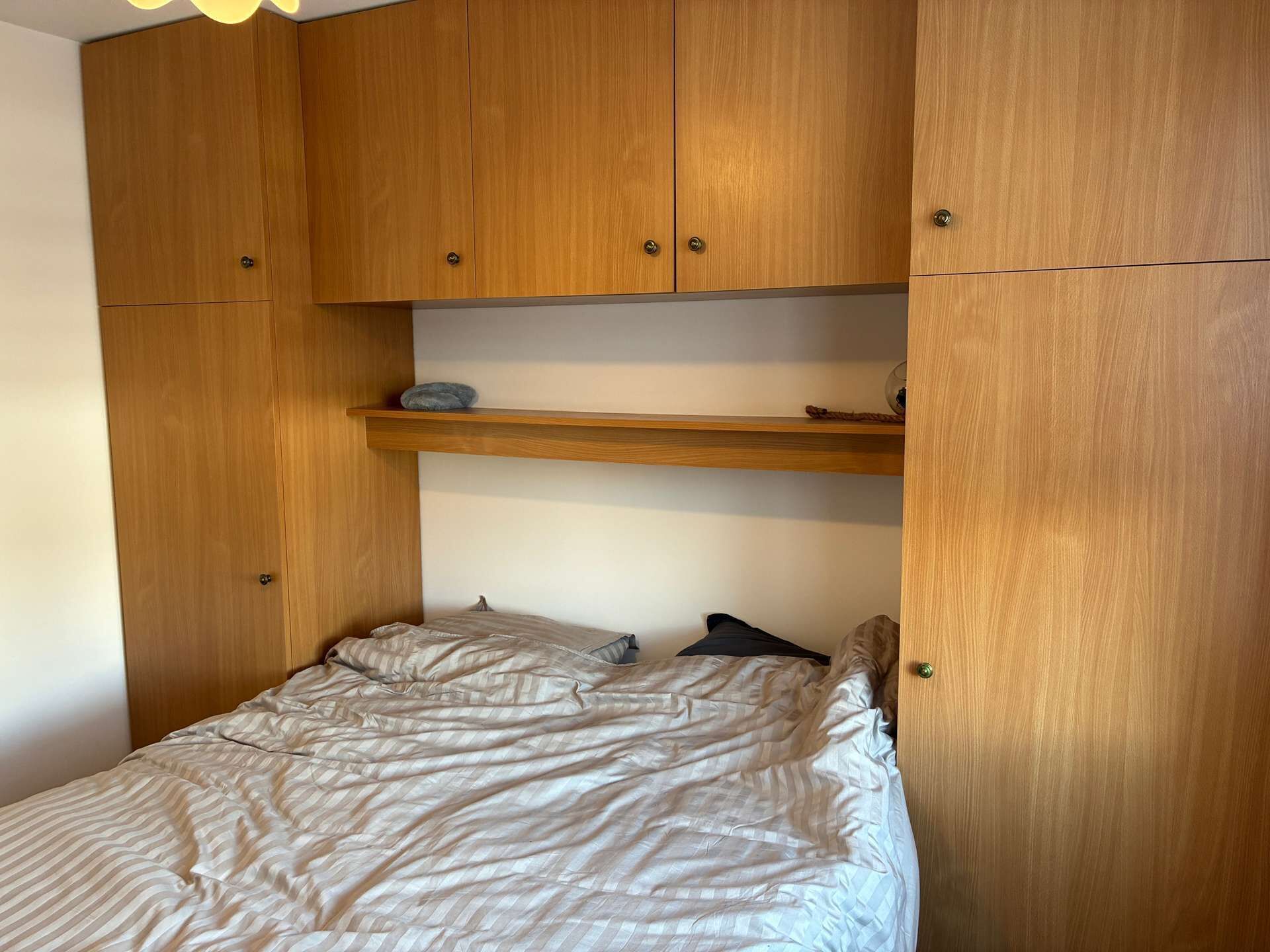 A bedroom with a bed, wooden wardrobe, and a shelf.