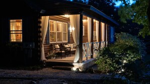A log cabin with a porch, a seating area with cushions, and a small garden. - Scenic, Dog-Friendly Log Cabin: Minutes to Lake Winnipesaukee, Gunstock Mountain (Gilford)