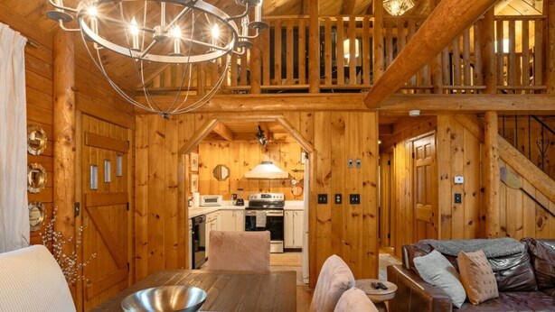 A wooden cabin interior with a dining area, kitchen, and a living room with a sofa. - Scenic, Dog-Friendly Log Cabin: Minutes to Lake Winnipesaukee, Gunstock Mountain (Gilford)