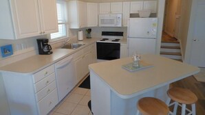Une cuisine compacte avec des meubles blancs, un four à micro-ondes, une cuisinière et un petit îlot central avec des tabourets.