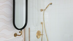 Ett badrum med ett vitt handfat, en spegel med svart ram, ett guldfärgat duschmunstycke och en duschhörna med glasväggar.
