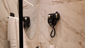 Un baño moderno con pared de mármol, inodoro negro, lavamanos blanco y un perchero para toallas.