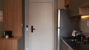 Una cocina moderna con refrigerador, estufa y cafetera. Hay una mesa de comedor de madera con sillas. Una puerta da a otra habitación.