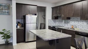 Eine moderne Küche mit dunklen Schränken, Edelstahlgeräten, einer Kücheninsel mit Granitplatte und einer gefliesten Spritzwand.