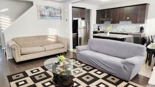 Ein Wohnzimmer mit einem beigefarbenen Sofa, einem grauen Sofa, einem Glastisch und einem Teppich mit Muster.