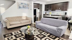 A living room with a beige sofa, a gray sofa, a glass coffee table, and a patterned rug. - Spacious A/C home, Garage Parking, Close Airport (Calgary)