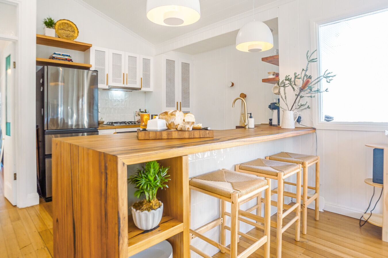 A modern kitchen with a wooden island, bar stools, a stainless steel refrigerator, and a window with a view.