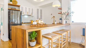 A modern kitchen with a wooden island, bar stools, a stainless steel refrigerator, and a window with a view.