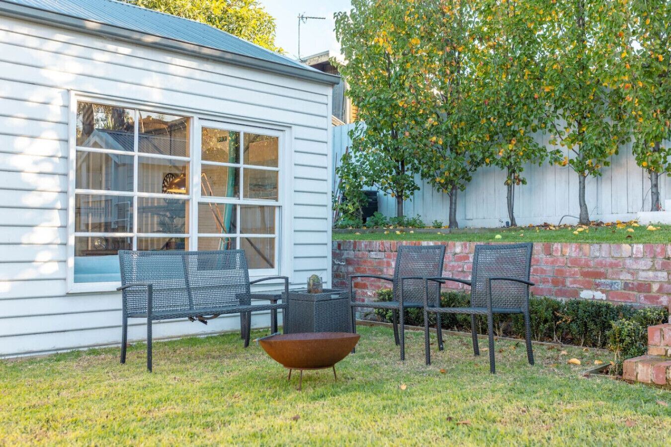 A house with a large window, a patio with chairs and a table, and a tree with fruit.