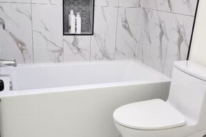 Ein Badezimmer mit einer weißen Badewanne, einer Toilette und einem Ablagefach mit Pflegeprodukten.