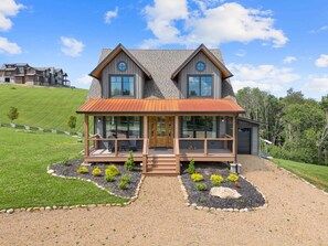 A two-story house with a covered porch, a front door, and a landscaped front yard. - Muscadine Meadow at Eagles Nest (Elk Park)