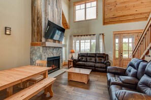 A living room with a fireplace, wooden furniture, a leather sofa, and a TV mounted on the wall. - Muscadine Meadow at Eagles Nest (Elk Park)