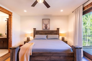 A bedroom with a large bed, wooden headboard, two bedside lamps, a wall-mounted painting of a deer, and a window with curtains. - It Was All a Dream at Eagles Nest - fireplaces, Springs (Banner Elk)