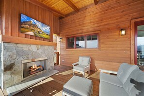 Eine Holzblockhütte mit Kamin aus Stein, einem aufgehängten Gemälde, einer Holzterrasse und einer Sitzgelegenheit.