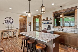 A kitchen with a large island, wooden bar stools, pendant lighting, and a view through the window. - Sunset Holiday at Eagles Nest - community amenities, pet friendly (Elk Park)