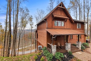 A wooden cabin with a porch, stone pillars, and a view of the surrounding forest. - Running Bear Lodge at Eagles Nest - community amenities (Banner Elk)