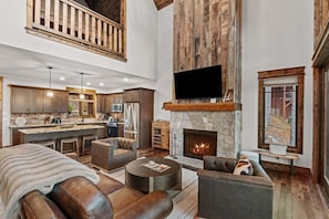 A spacious living area with a fireplace, leather sofas, a kitchen with wooden accents, and a large TV. - Running Bear Lodge at Eagles Nest - community amenities (Banner Elk)