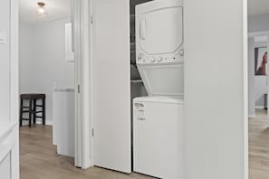 Ein Waschraum mit einer weißen Waschmaschine, einem Holzschemel und einem weißen Schrank.