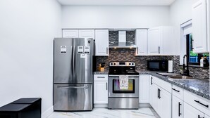 A modern kitchen with stainless steel appliances, white cabinets, and a tiled backsplash. - HARD ROCK OASIS - 3BR Pool Home + Game Room (Miami)