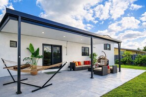 A modern outdoor patio with a hammock, seating area, and potted plants. - HARD ROCK OASIS - 3BR Pool Home + Game Room (Miami)