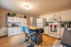 A modern kitchen with white cabinets, a stainless steel sink, a microwave, an oven, and a bar stool.