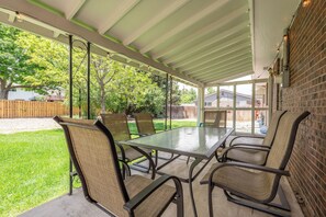 A covered patio with a glass table and chairs, a brick wall, and a view of a backyard.