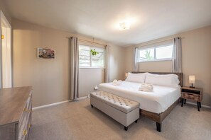 A bedroom with a bed, a bench, a nightstand, a wall-mounted light, and a window with curtains.