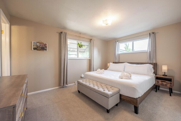 A bedroom with a bed, a bench, a nightstand, a wall-mounted light, and a window with curtains.