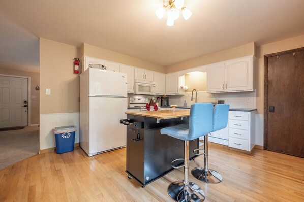A kitchen with a refrigerator, microwave, stove, and a bar stool.