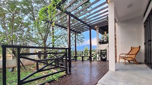 Un espace extérieur abrité, doté d’une terrasse en bois, d’une rambarde en métal et d’une seule chaise en osier.