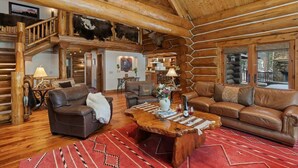 A log cabin interior with a wooden staircase, leather sofas, a wooden coffee table, and a dining area. - Abode at Forest Edge, luxury log home, hot tub (Wilson)