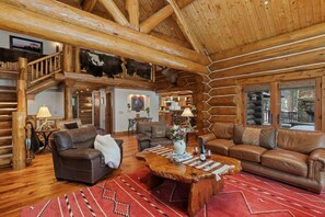 A log cabin interior with a wooden staircase, leather sofas, a wooden coffee table, and a dining area. - Abode at Forest Edge, luxury log home, hot tub (Wilson)